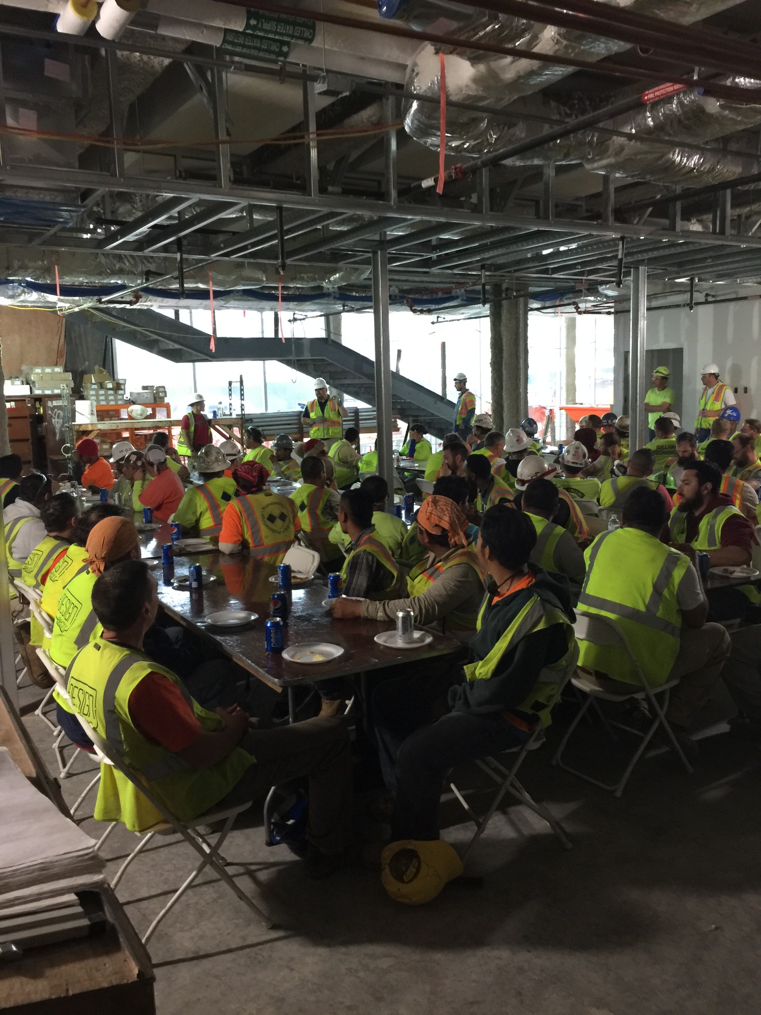 Construction crew members in high-visibility clothing gathered at tables inside an active building site.